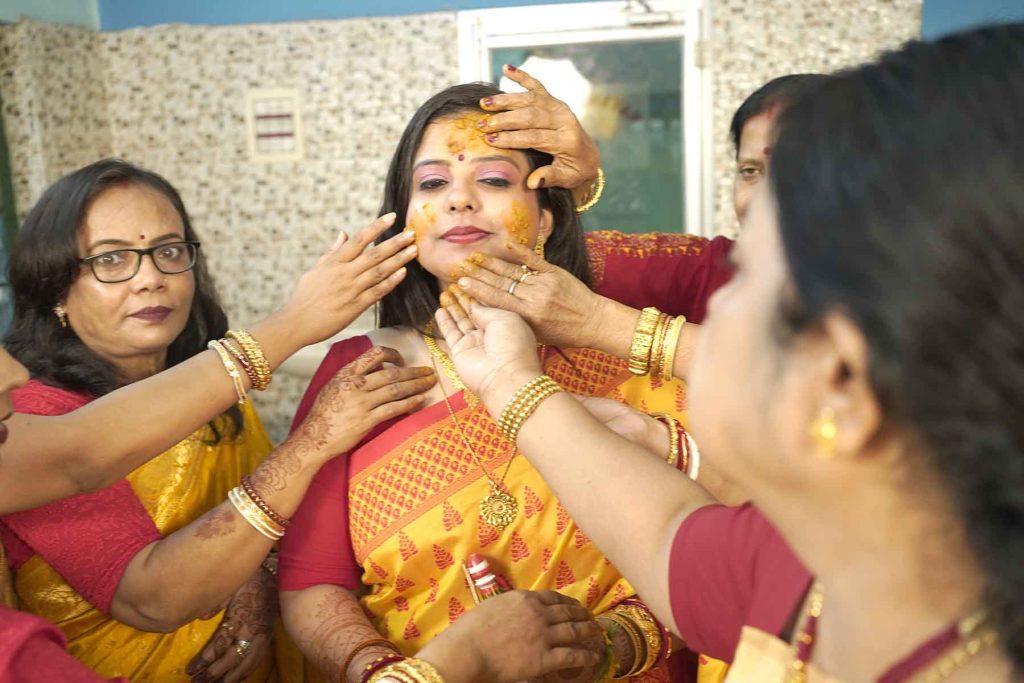 A joyful moment of applying turmeric paste on the bride's face during the traditional Bengali Gaye Holud ceremony.